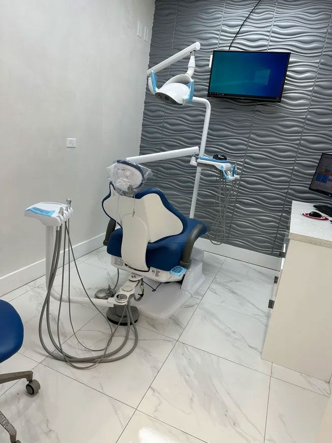 Dental chair and equipment in a modern office with blue and white accents, a TV, and textured wall.