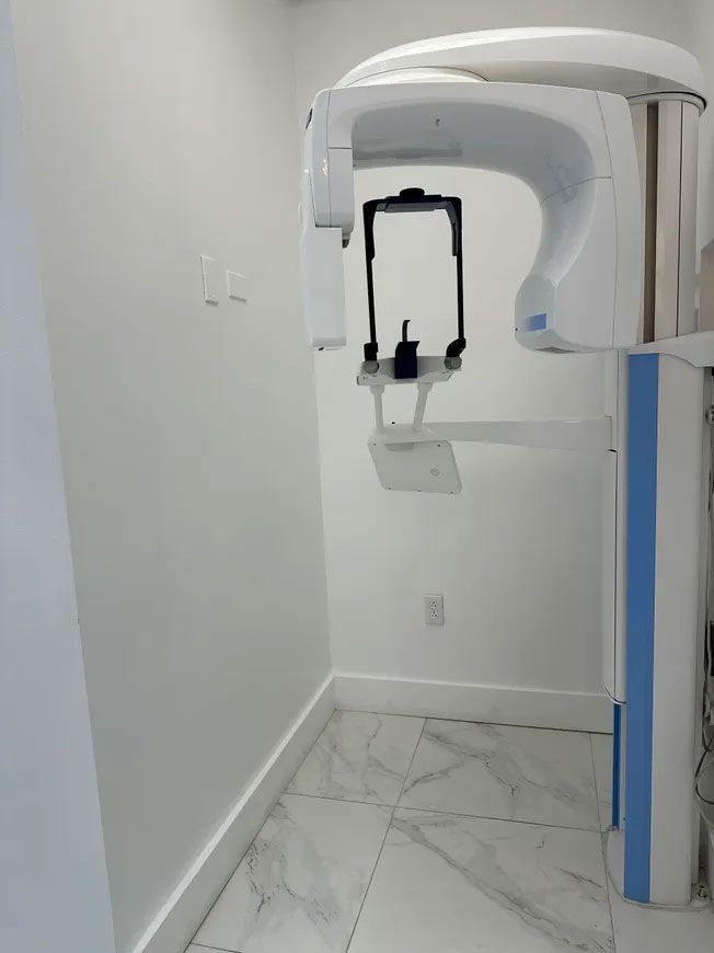 Dental panoramic X-ray machine in a white room with a marble floor. The machine is mostly white with blue accents.