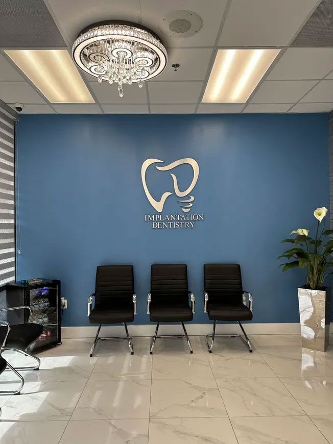 Dental office waiting area with blue wall, logo, black chairs, and decorative lighting.