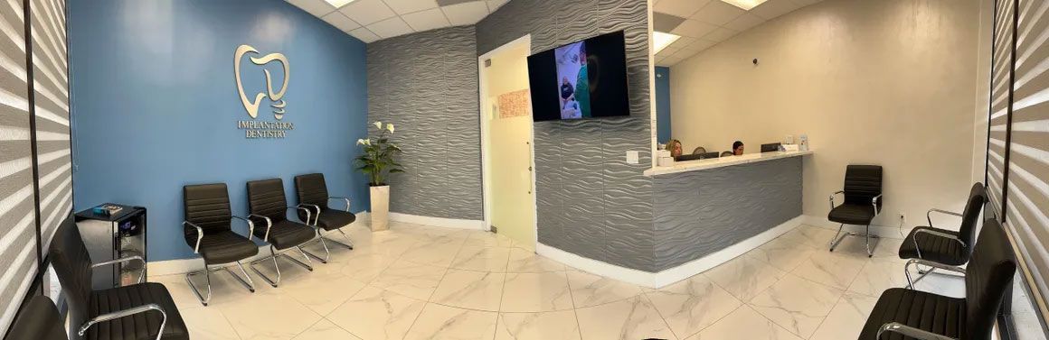 Dental office waiting room. Blue and gray walls, black chairs, a reception desk, and a large logo are visible.
