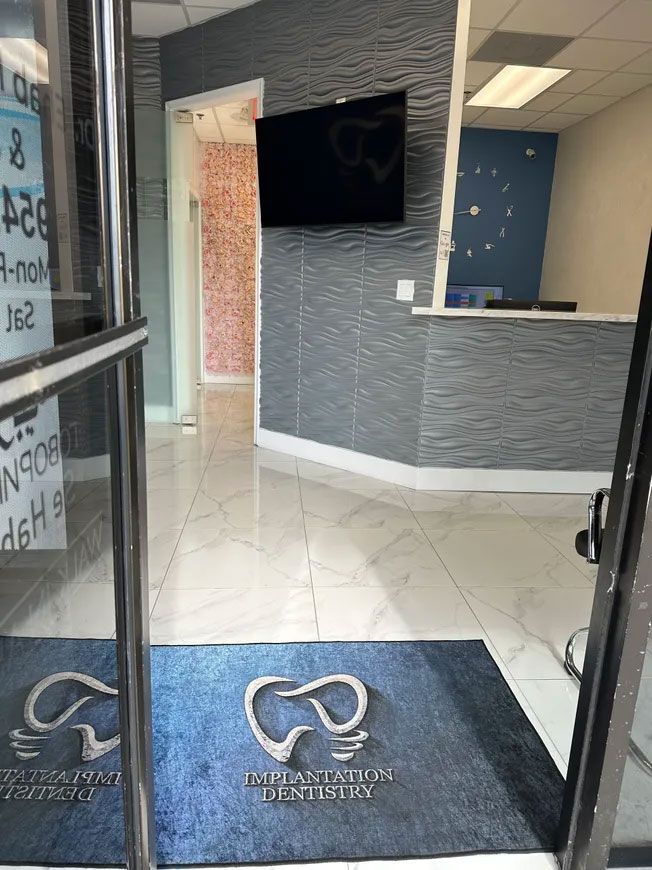 Entrance to a dental office with blue door mat, grey textured walls, and a waiting area.
