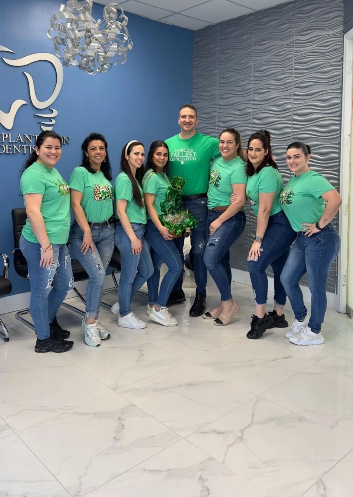 Group of people in matching green shirts and jeans at a dental office, posing for a photo.