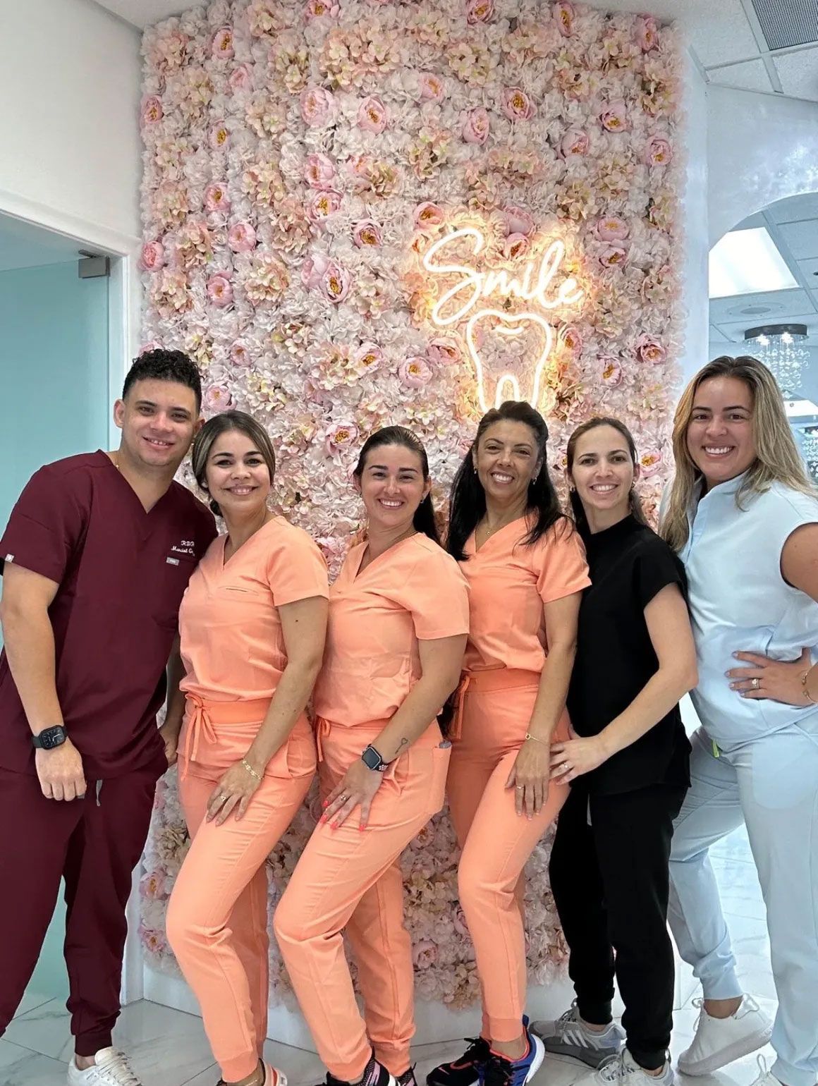 Dental team posing; peach scrubs, maroon scrubs, floral wall, neon 