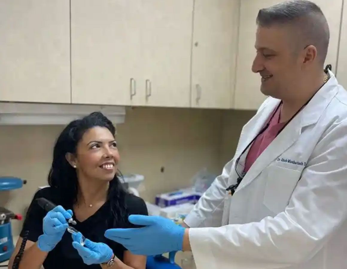 A person and a doctor in a medical office, smiling and discussing a tool. The person wears gloves.