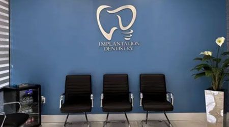 Waiting area with blue wall, dental logo, three black chairs, and a plant.