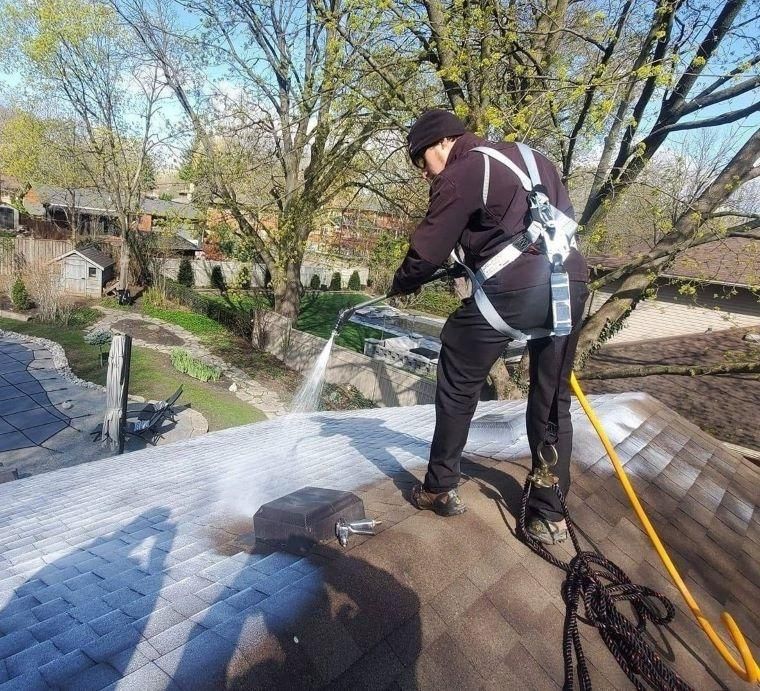 A man is cleaning a roof with a high pressure washer.