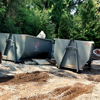 Two dumpsters are parked next to each other in a dirt field.