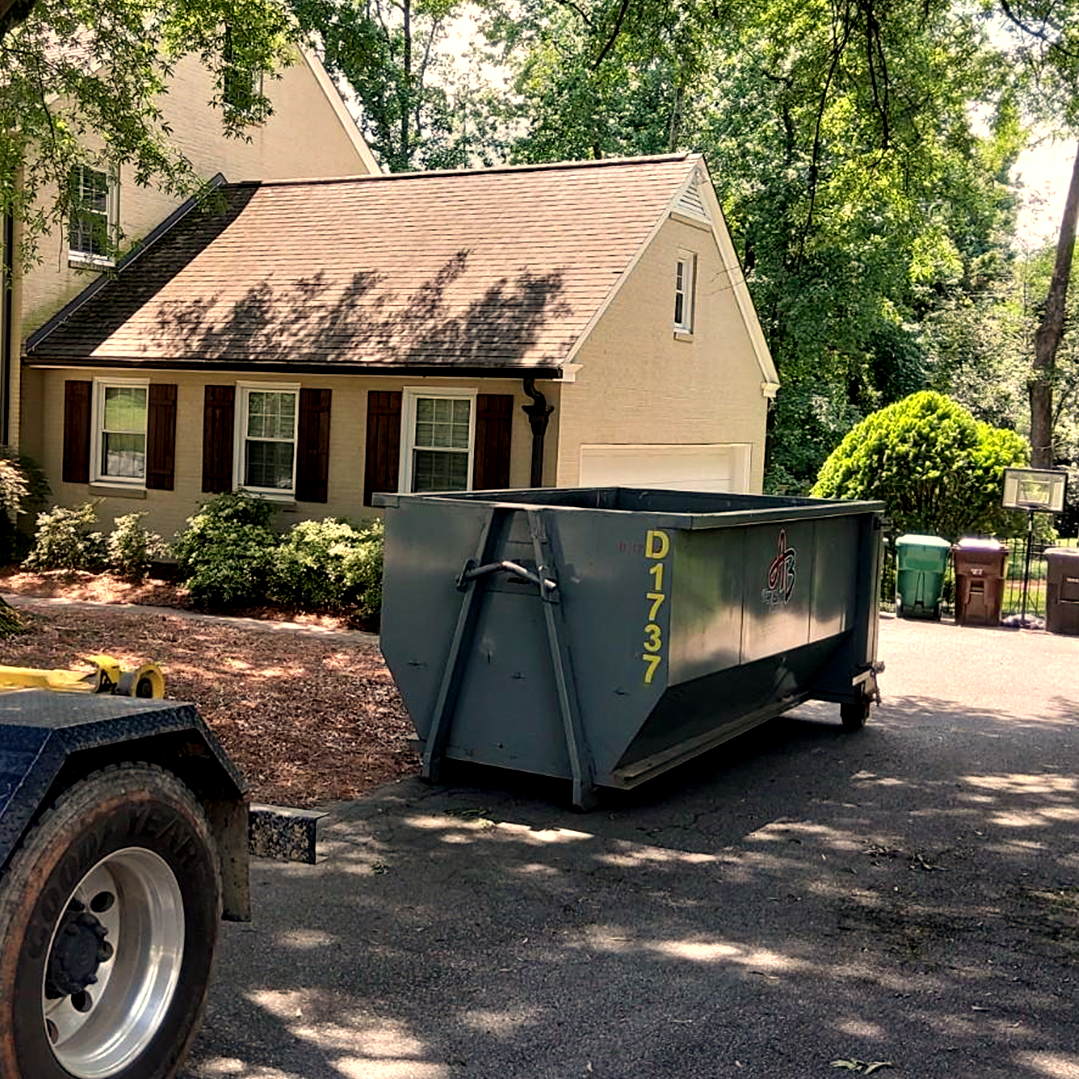 A dumpster on a trailer is parked in front of a house.