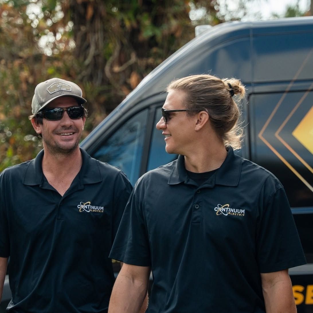 Two people in dark polos and sunglasses standing beside a van outdoors