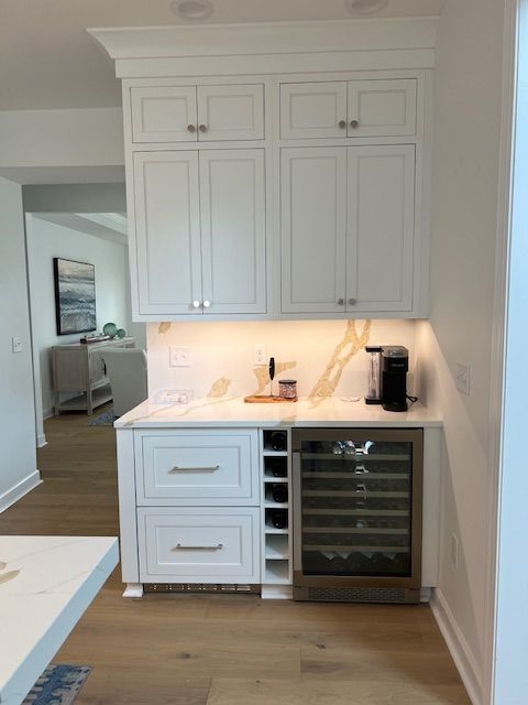 White wet bar with upper cabinets, countertop, two drawers, vertical wine rack, and a built-in beverage refrigerator.