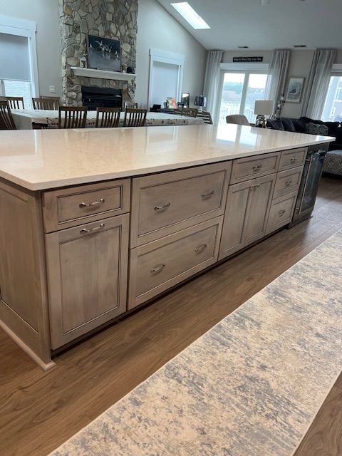 Large kitchen island with light gray wooden cabinets and a white countertop, positioned in an open-concept living area.