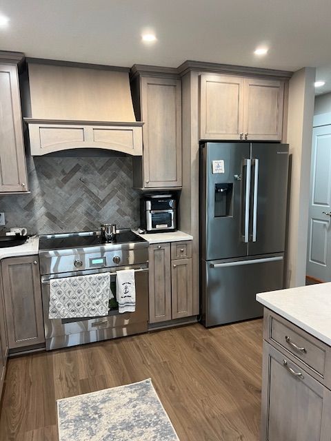A modern kitchen featuring light-wood cabinets, stainless steel appliances, a herringbone backsplash, and wood flooring.