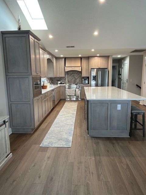 Modern kitchen with grey cabinets, light wood flooring, a white countertop island, and a long rug on the floor.
