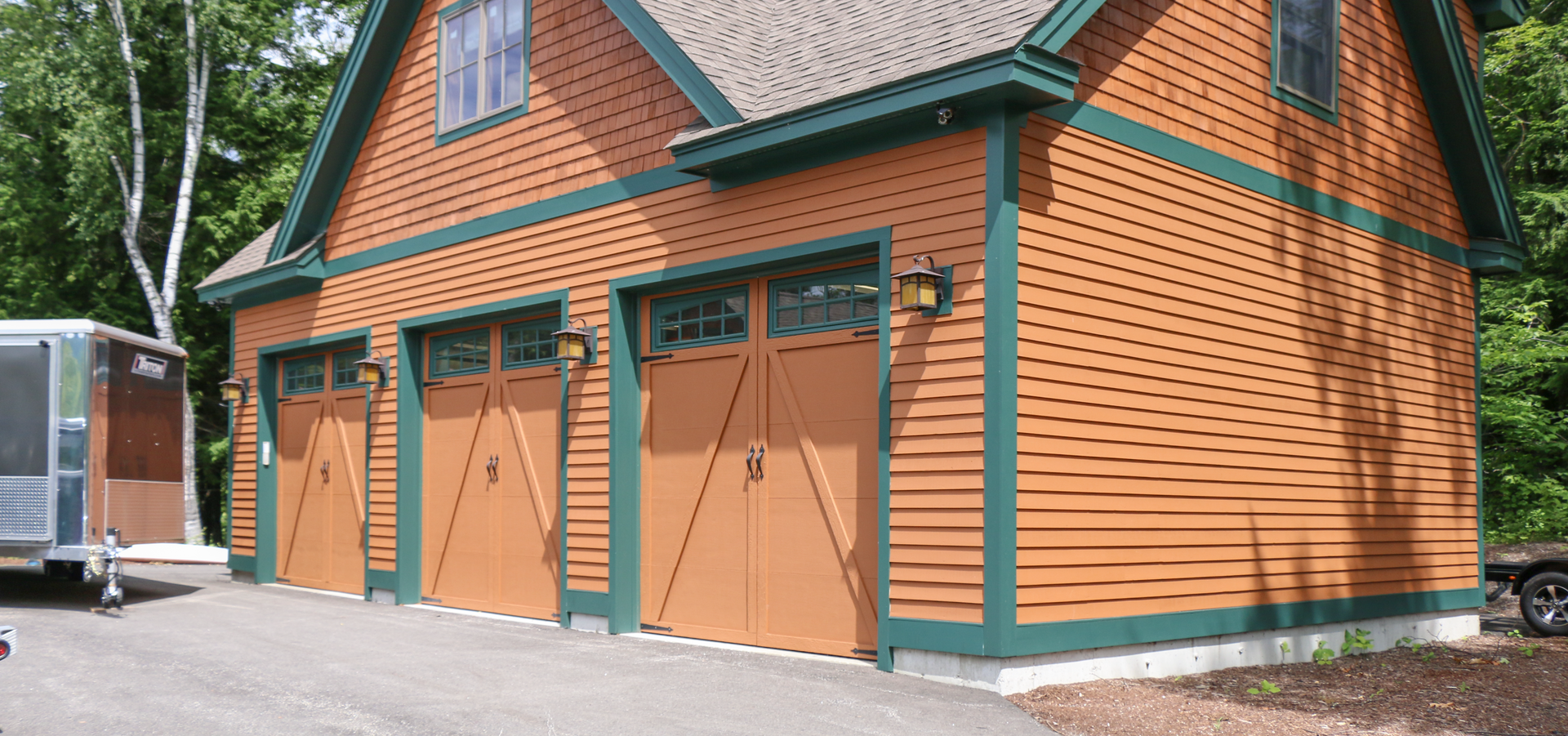 A large orange garage with green trim and a trailer parked in front of it.