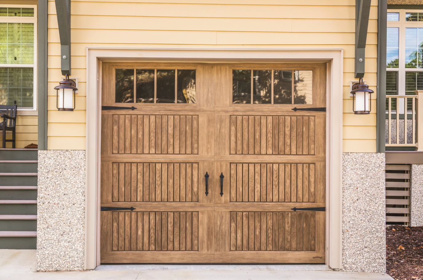 A wooden garage door is sitting in front of a yellow house.