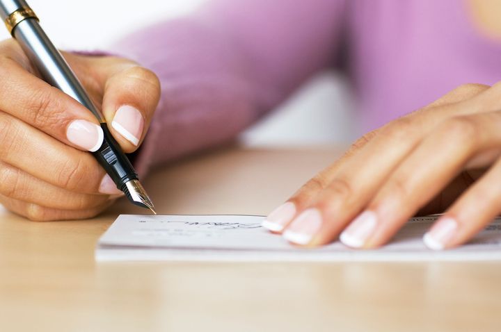 A woman is writing a check with a fountain pen