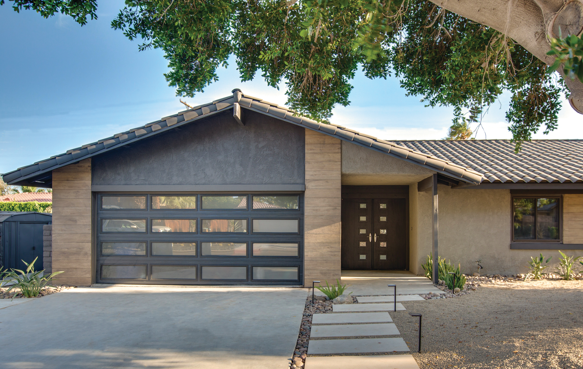 A house with a black garage door and a tree in front of it