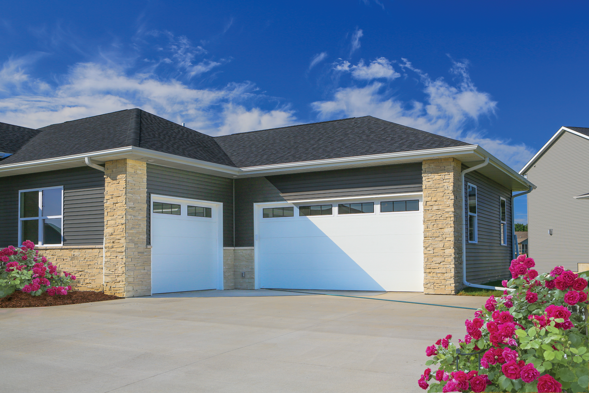 A house with two garage doors and flowers in front of it