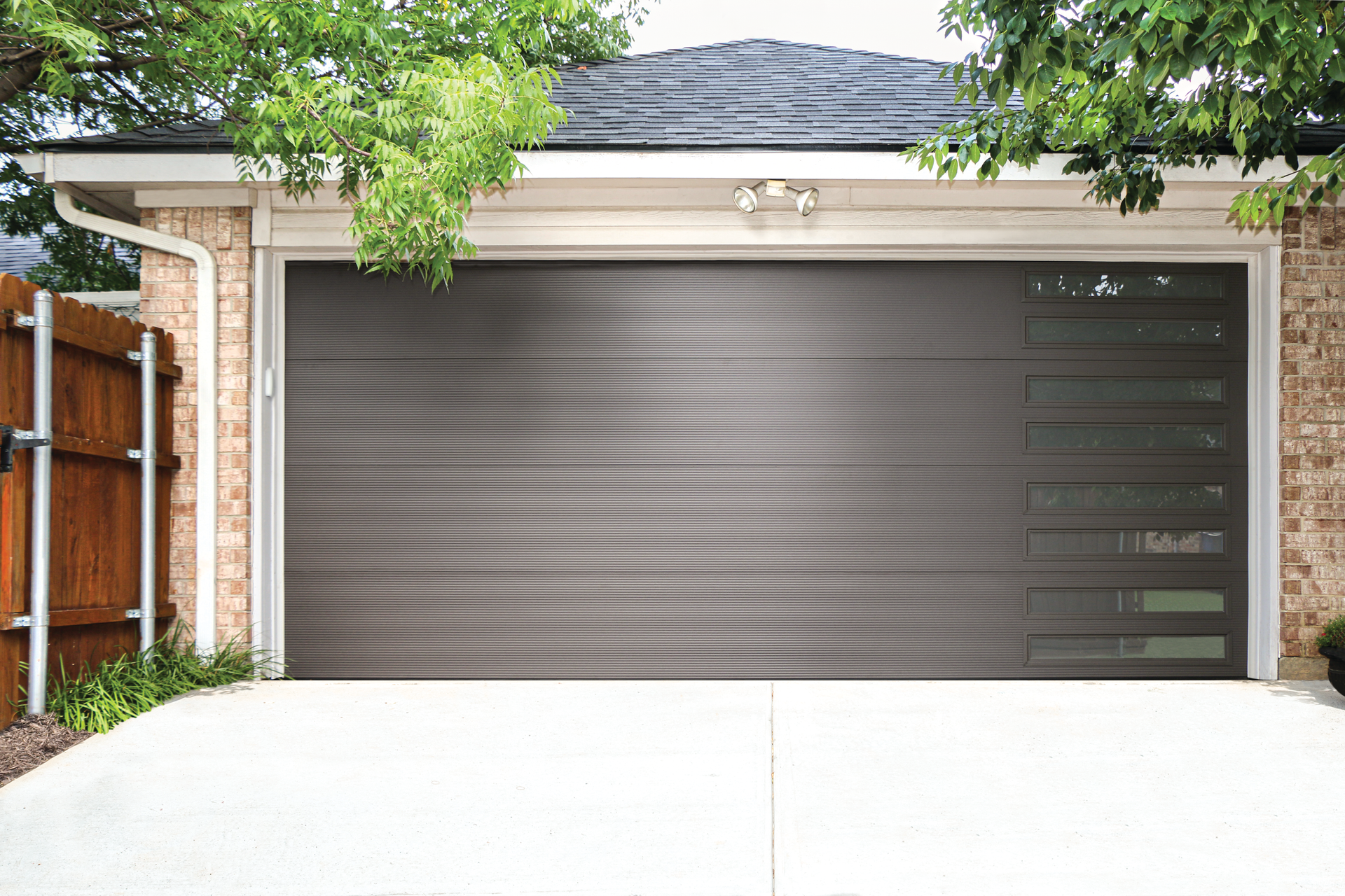 A brick house with a gray garage door and a wooden fence.