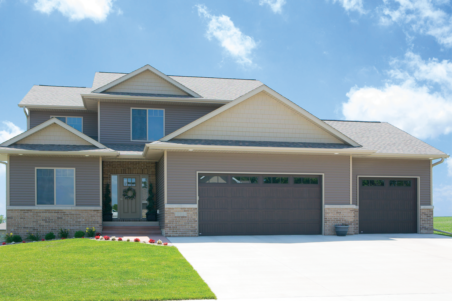 A large house with three garage doors is sitting on top of a lush green field.