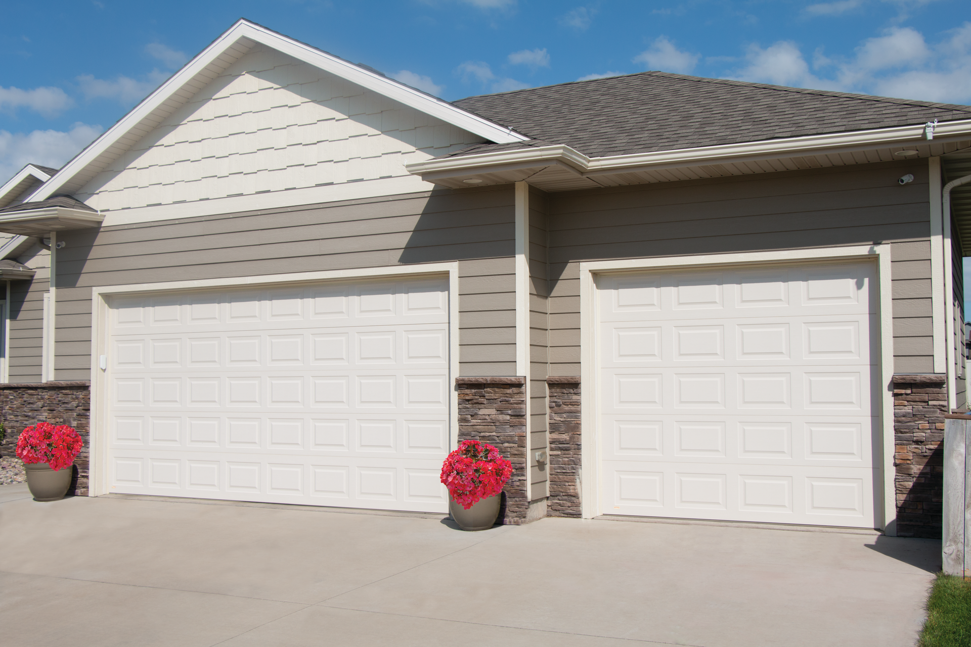 A house with two garage doors and two potted plants in front of it.