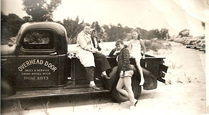 A black and white photo of people sitting in the back of an overhead door truck