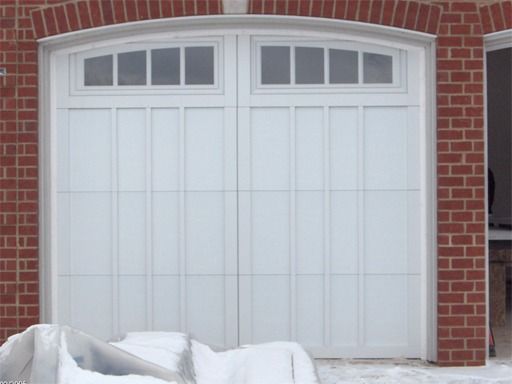 A white garage door with a brick wall behind it
