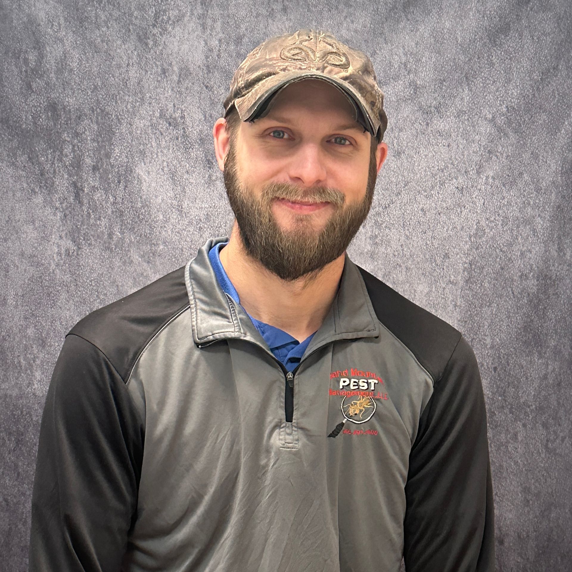 Man with beard and bald head smiles in front of a brick wall, wearing a dark shirt.