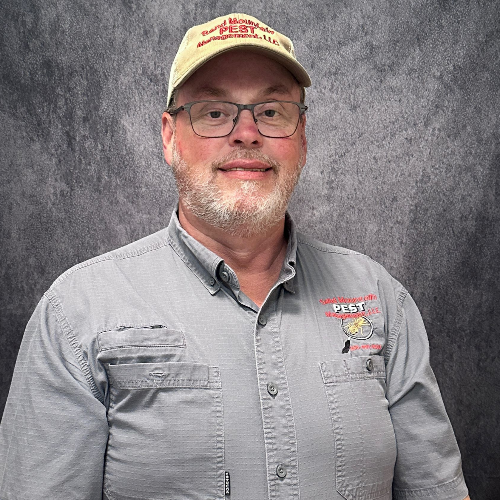 Man wearing glasses and a hat, smiling, with a pest control logo on his shirt.