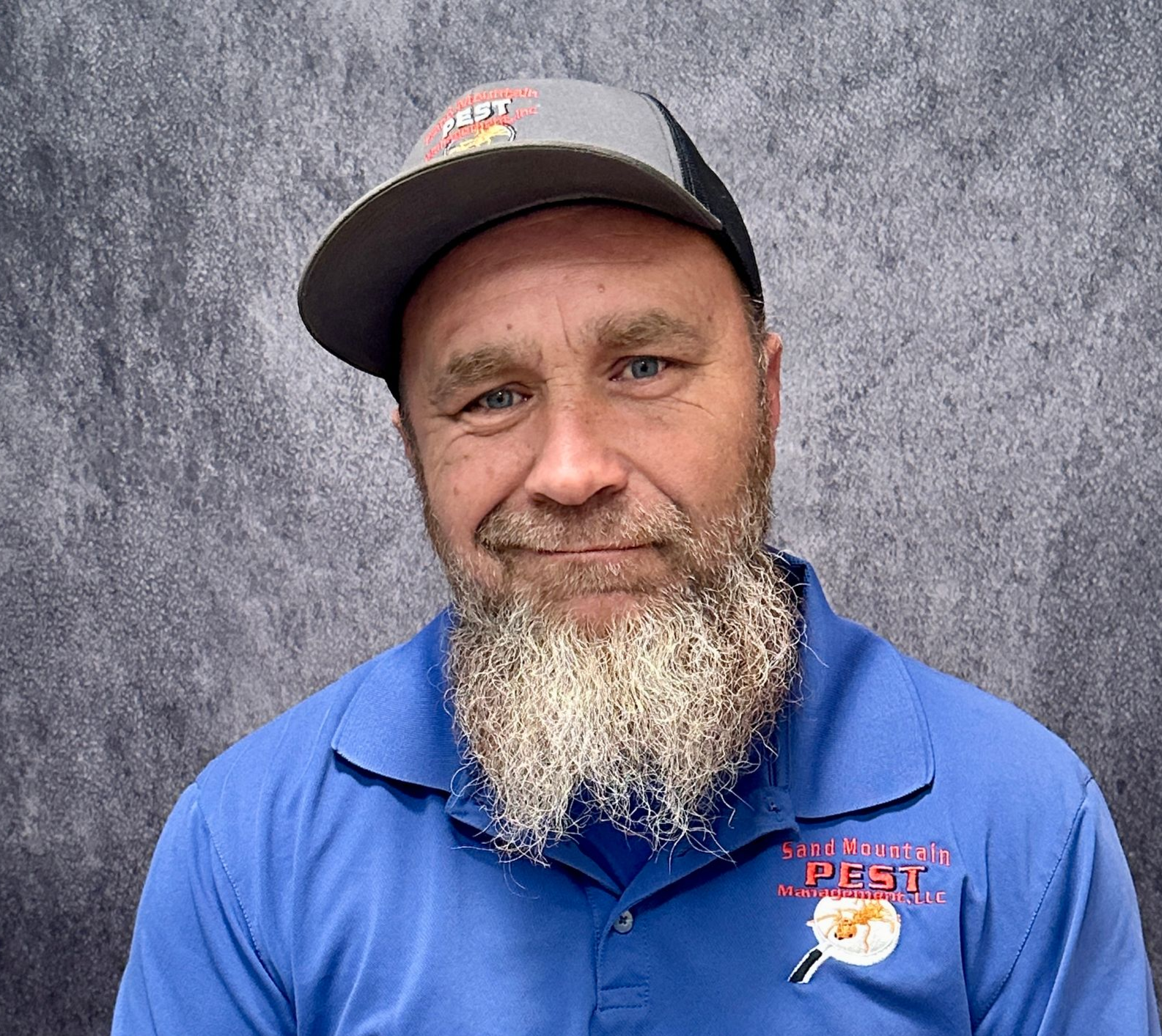 Man wearing a cap and blue shirt smiling in front of a brick wall.