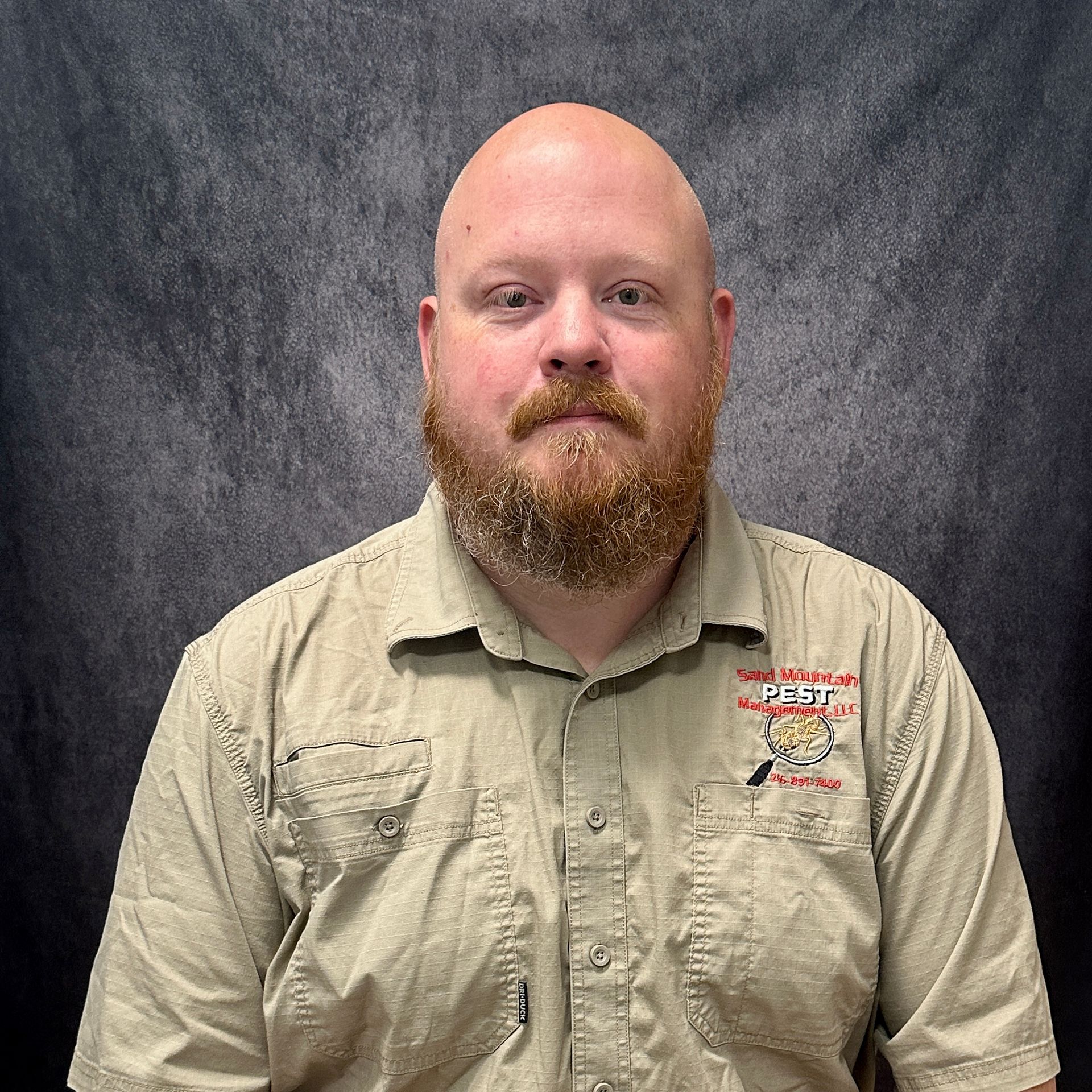 Bald man with a red beard in a vehicle. He's wearing a blue shirt and looking at the camera.