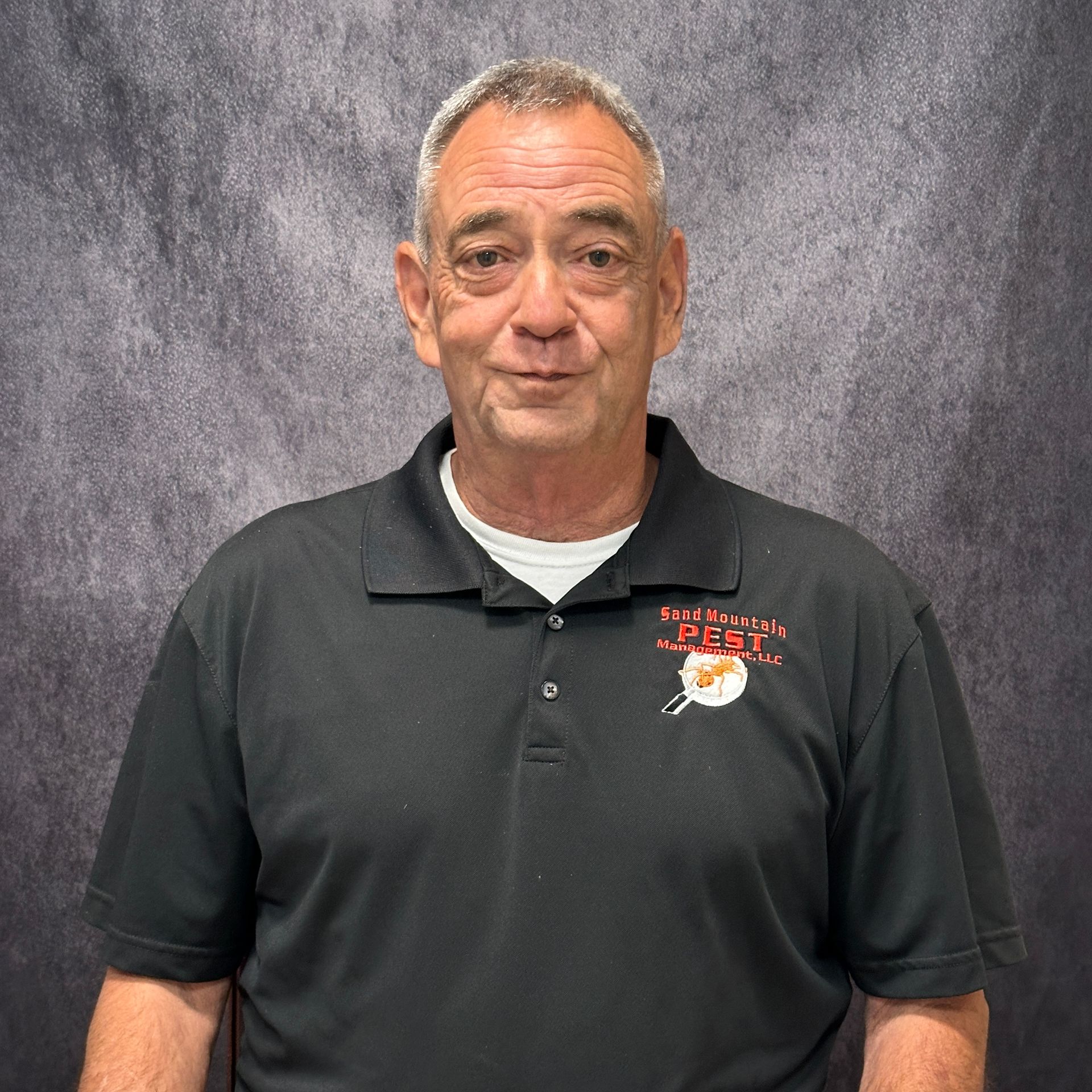 Man in black polo shirt stands in front of a brick wall.