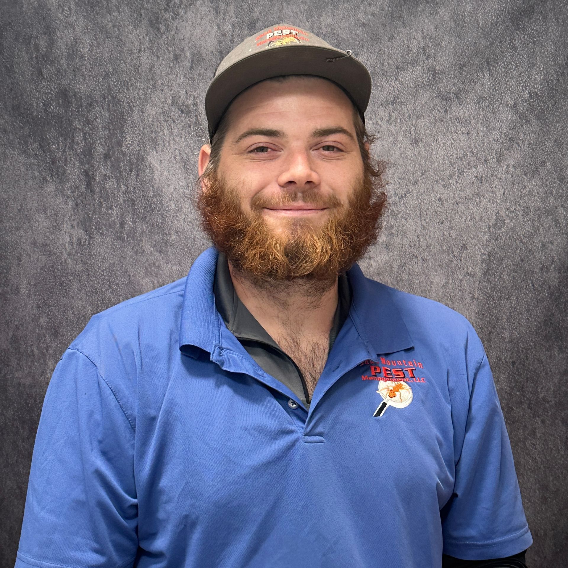 Man with beard and hat, wearing a black shirt, smiles in front of a sign.