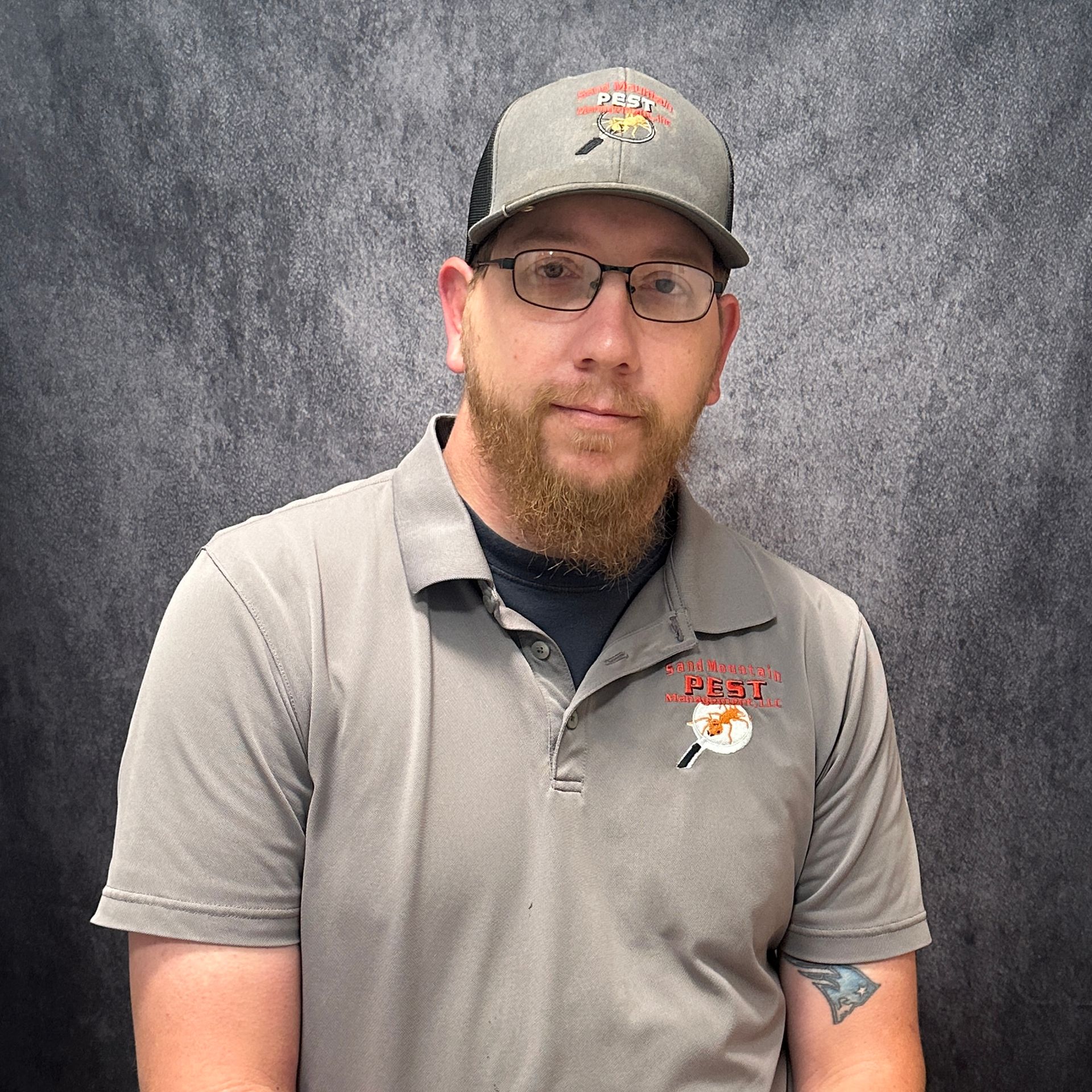 Man in glasses and cap with a beard, in front of a brick wall.