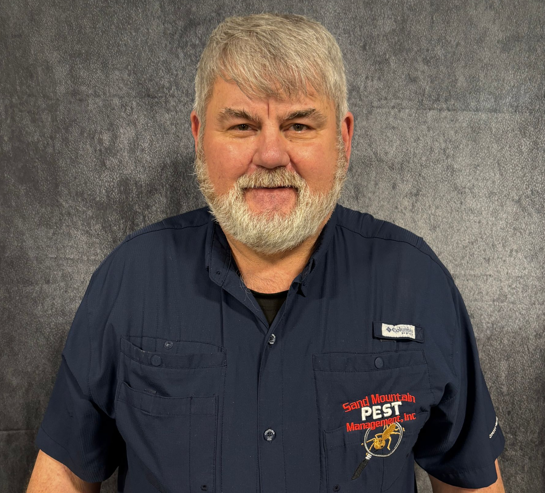 Man with salt and pepper hair and mustache stands in front of a brick wall.