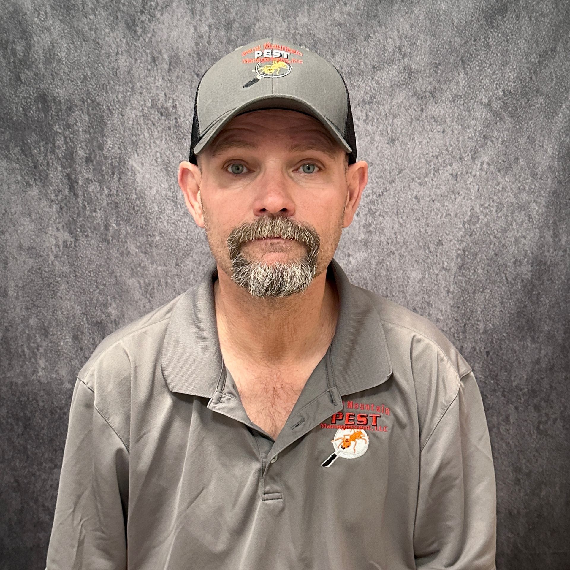 Man with a goatee smiling in front of a brick wall, wearing a black shirt with a company logo.
