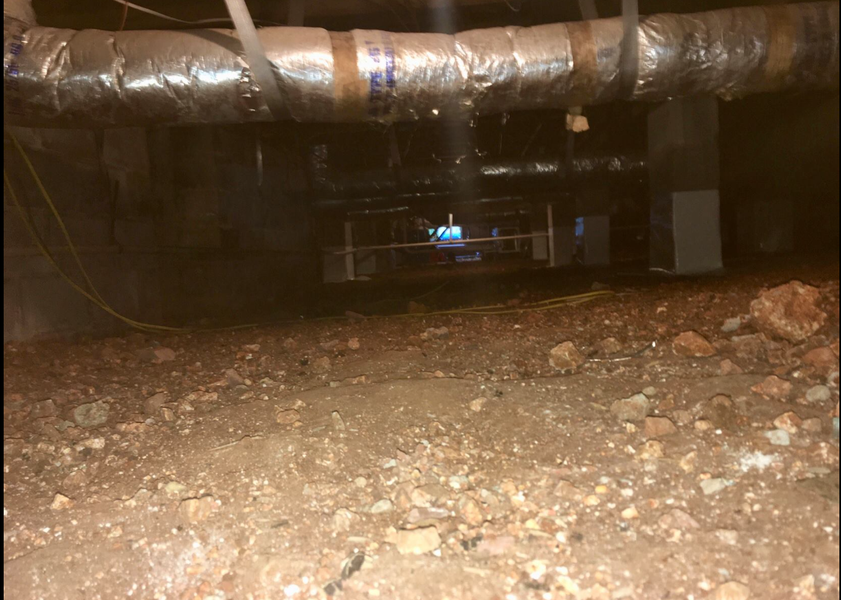 Crawlspace with dirt floor, HVAC ductwork, and equipment visible in dim lighting.