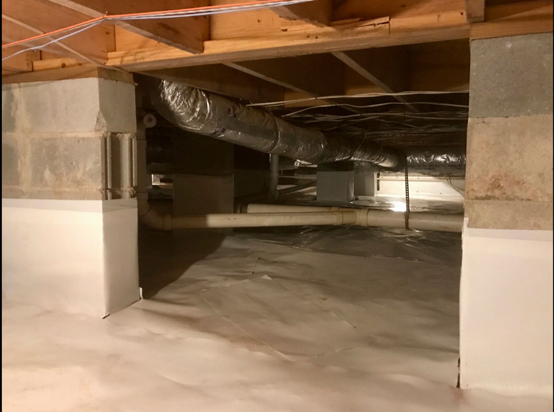 Crawl space with white vapor barrier flooring. Wooden beams, ductwork, and utility lines are visible.