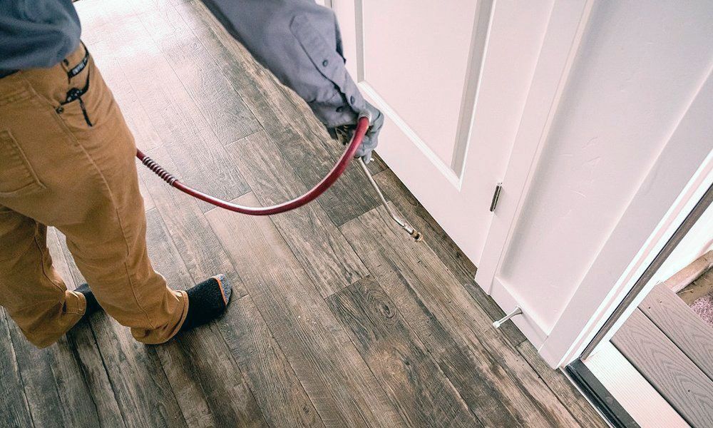 Person using a red air hose near white door trim on a wood-look floor.