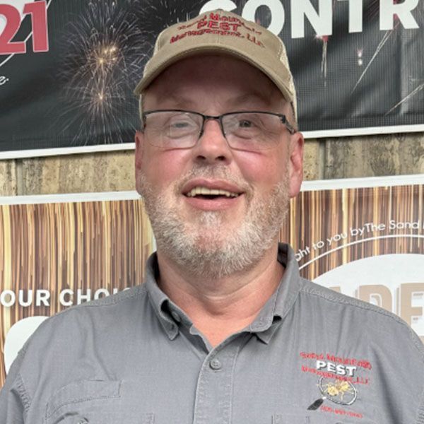 Man wearing glasses and a hat, smiling, with a pest control logo on his shirt.