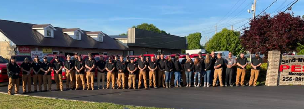 A large group of people in matching work uniforms standing in front of a building and red vehicles.