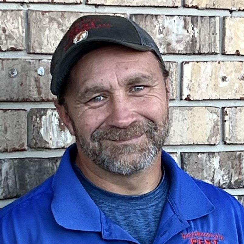 Man wearing a cap and blue shirt smiling in front of a brick wall.