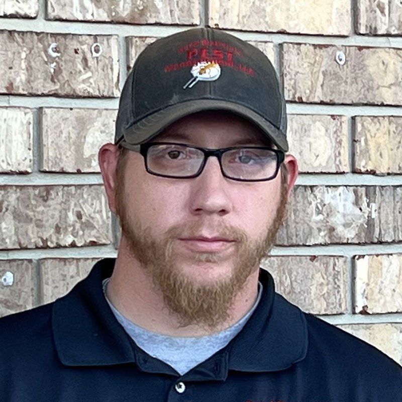 Man in glasses and cap with a beard, in front of a brick wall.