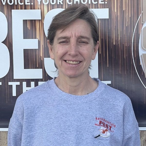 Woman in gray sweatshirt smiles in front of a sign; logo on the sweatshirt: 