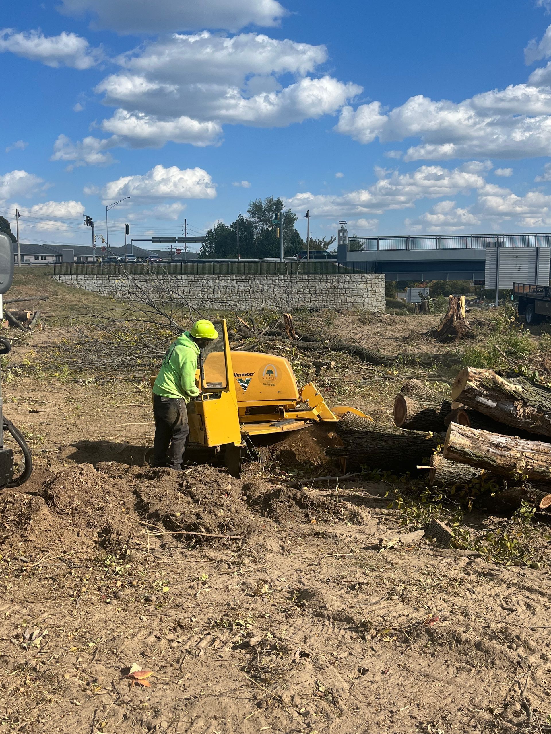 A person operating a yellow stump grinder on a construction site, under a blue sky.