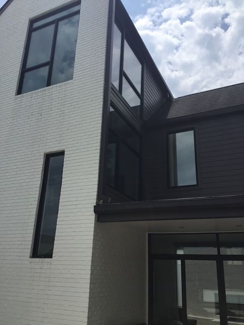 Modern two-story building with white brick and dark gray siding. Large windows, cloudy sky.