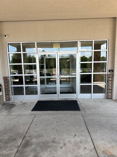 Glass doors of a building with white frames. A black doormat sits in front.