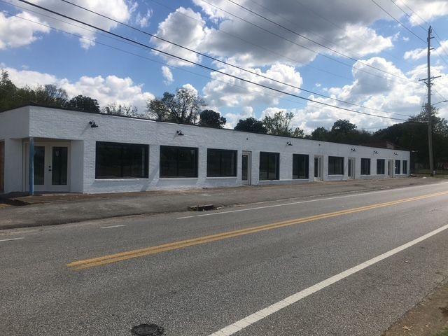 White commercial building with large windows along a road, under a blue sky with clouds.