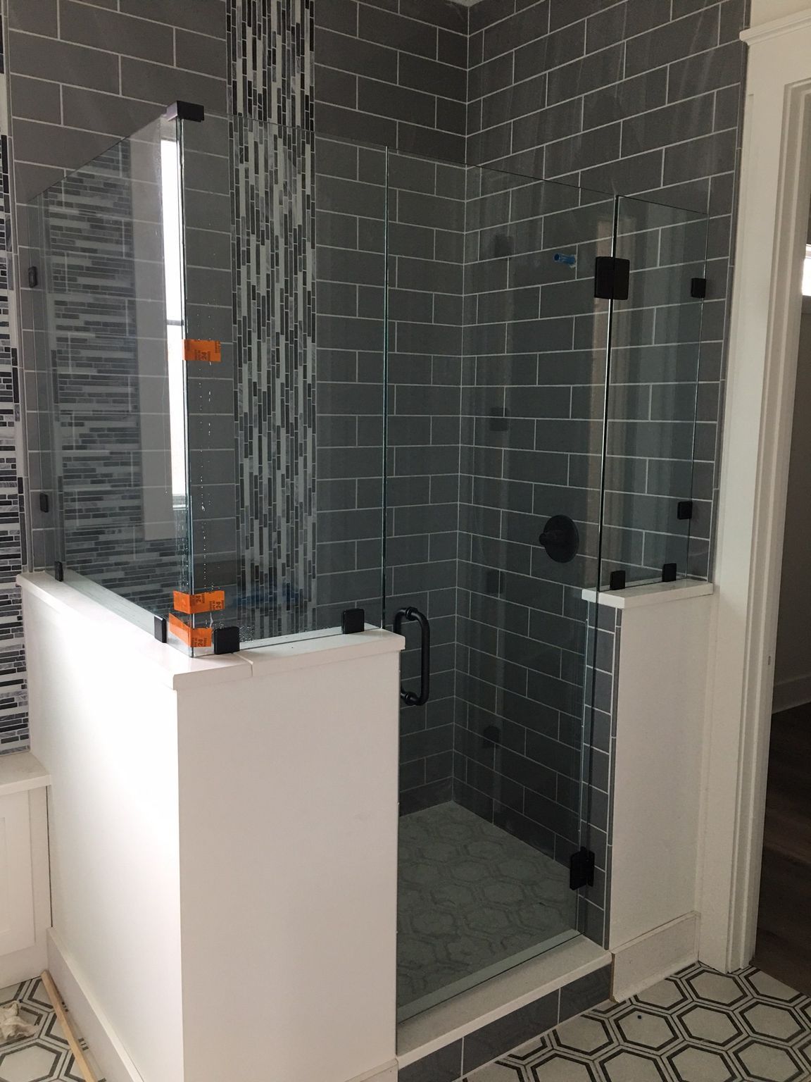 A modern bathroom with a gray tile shower, glass doors, and white walls.