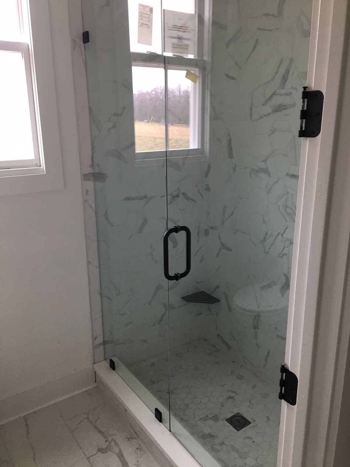 Glass shower with marble tile, black fixtures. Window in the back.